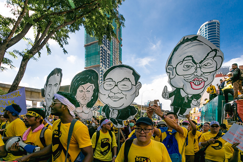 Protesters hold placards with caracature depicting Najib Razak, Rosmah Mansur, Jho Low.
